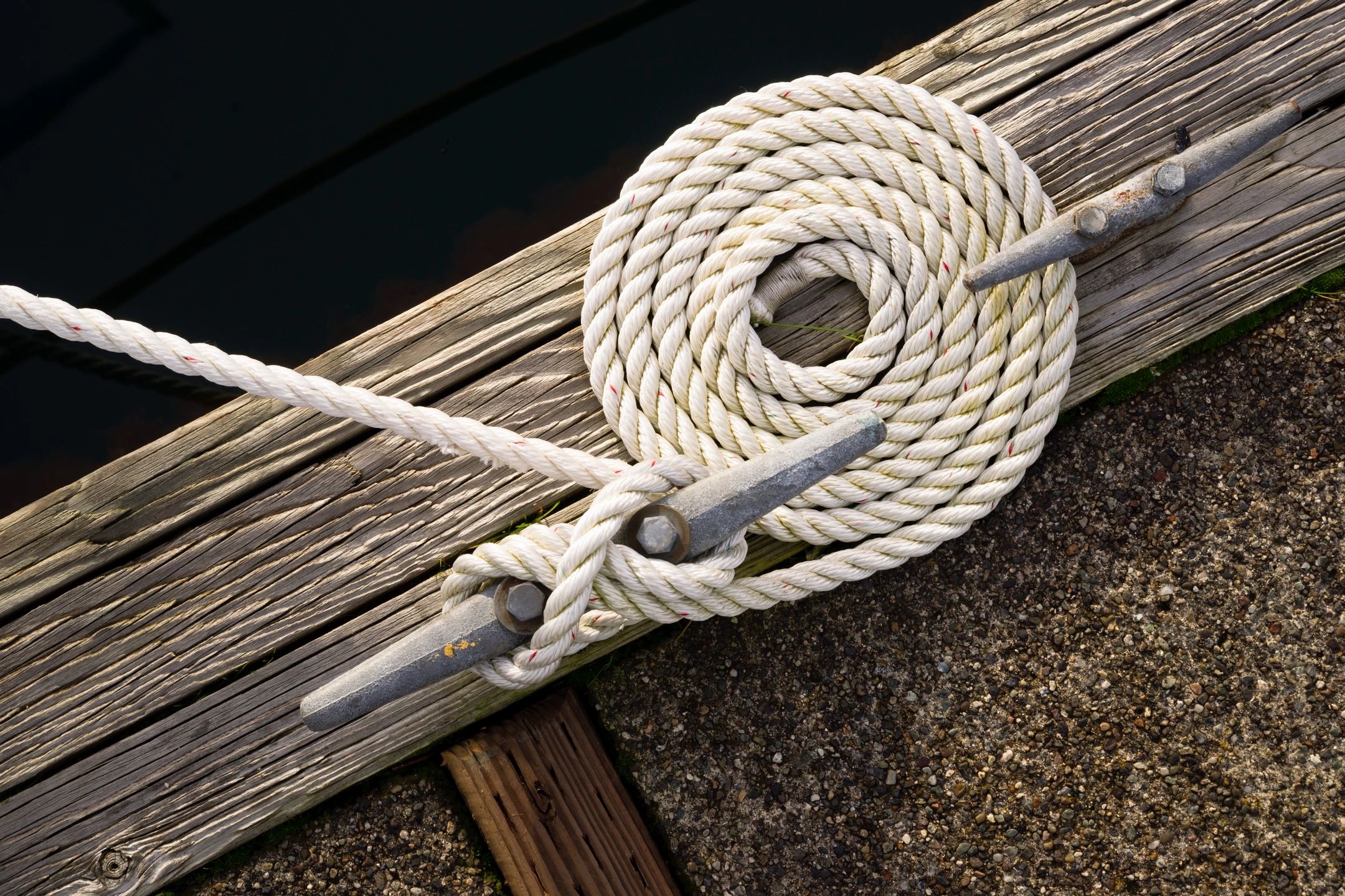 A rope tied to two metal rings on the side of a dock.