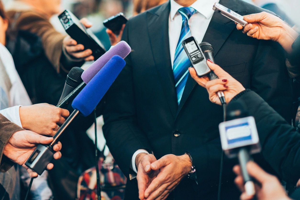 A man in a suit and tie surrounded by microphones.